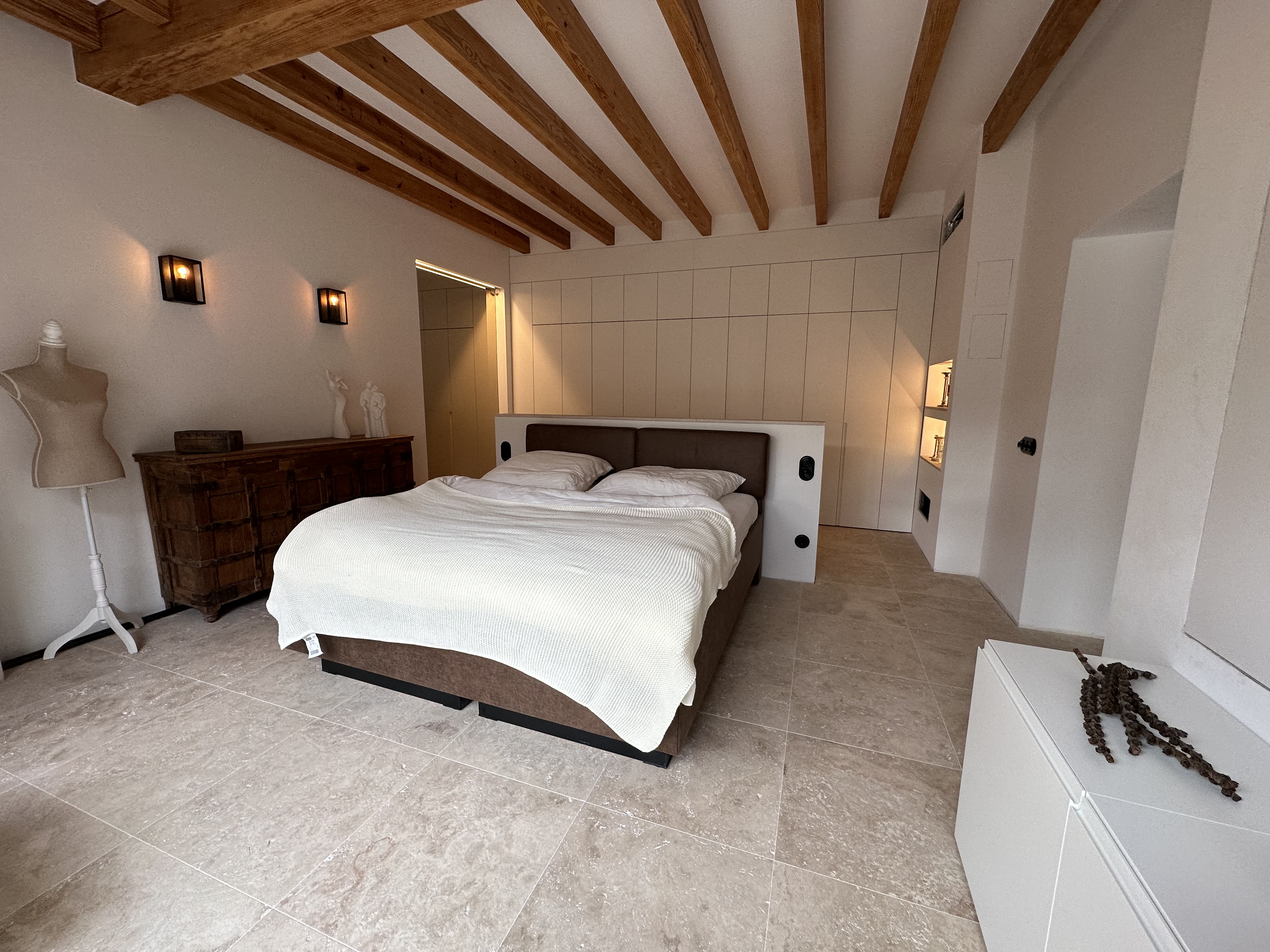 Dormitorio principal con vigas de madera centenaria y suelo de travertino